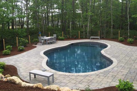 A kidney shaped swimming pool with extensive patio and plantings