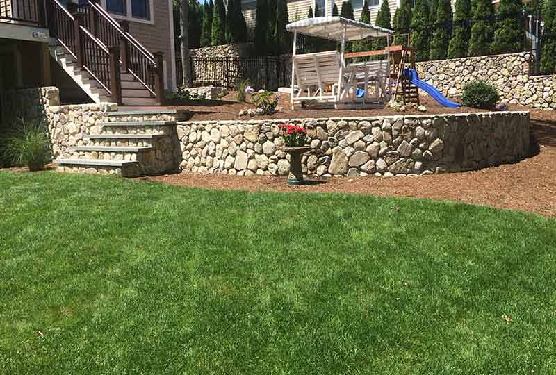 A full lawn below a retaining wall and deck with child play area